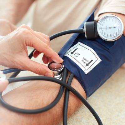 Doctor taking the blood pressure of a patient. Adult holding a red heart with a heartbeat traced in his hand.