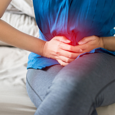 A close-up of a woman’s abdomen and pelvis. She is clutching her pelvis and bending over in pain.